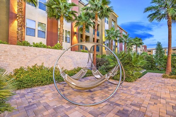 Pool area with stone paver patio, hammock stand, lush landscaping, and tall palm trees at Inspire Apartments in Northwest Las Vegas