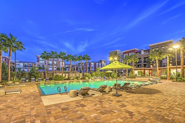 Pool area at Inspire Apartments in Northwest Las Vegas with stone paver patio, lounge chairs, day beds, umbrellas, and tall palm trees.