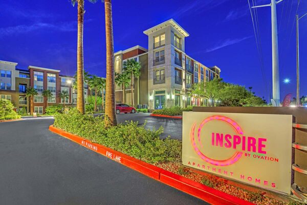 Inspire Apartments in Las Vegas entrance with lighted sign, lush landscaping, and tall palm trees.