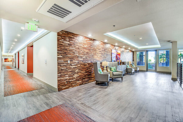 Mezzanine lounge at Inspire Apartments in Las Vegas with plush chairs, tables with lamps, artwork, and railing overlooking clubroom.