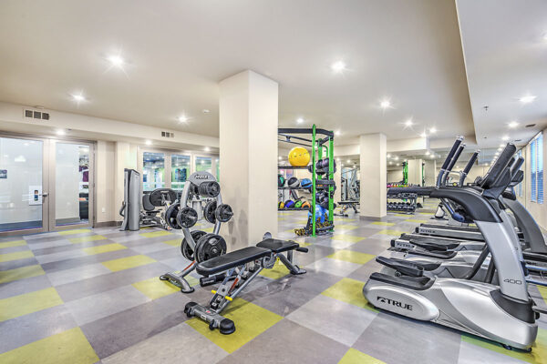 Fitness center at Inspire Apartments in Las Vegas with cardio machines, weight equipment, tile floor, and bright lights.