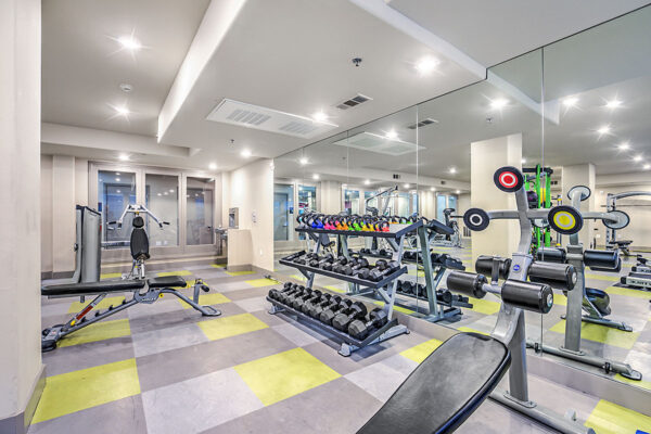 Fitness center at Inspire Apartments in Las Vegas with cardio machines, weight equipment, tile floor, and mirror wall.