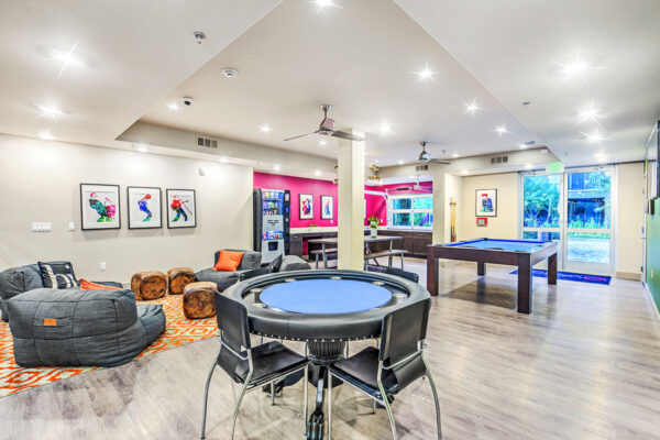 Game room with pool and poker tables, plush chairs, vending machine, and pop art posters at Inspire Apartments in Northwest Las Vegas