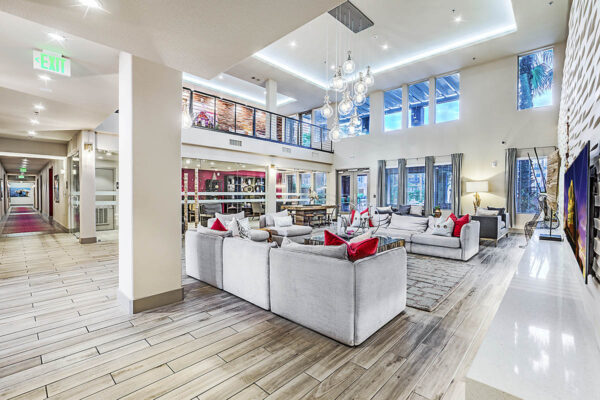 Clubroom at Inspire Apartments in Las Vegas with wood tile floor, plush couches, glass light fixture, large windows, and mezzanine.