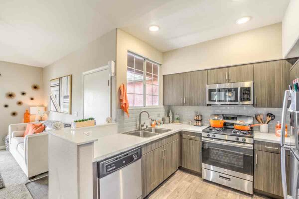 Kitchen with wood floor and cabinets, light counters, stainless steel appliances, and tiled backsplash.