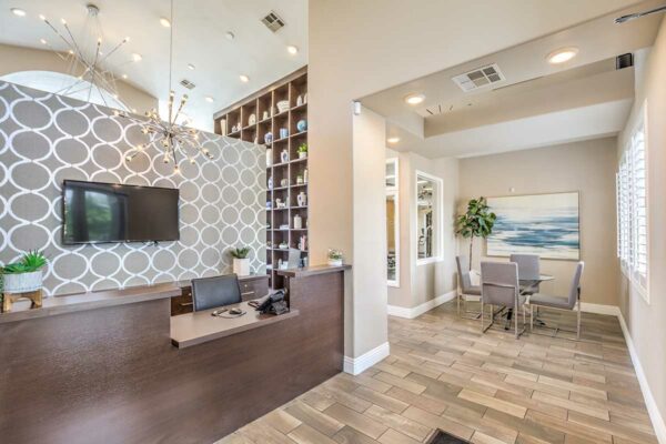 Lobby with wood style floor, desk with computer and TV, and table with chairs and artwork.
