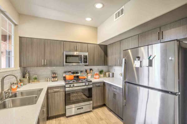 Kitchen with wood floor and cabinets, light counters, stainless steel appliances, and tiled backsplash.