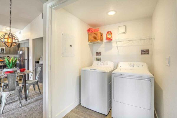Laundry room with washer, dryer, and shelf with linens and soap.