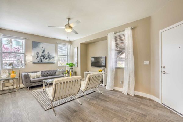 Living room with wood floor, plush seating, ceiling fan, TV, and artwork.
