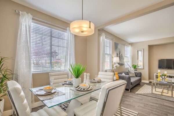 Dining room with glass table, plush leather chairs, light fixture, and large windows.
