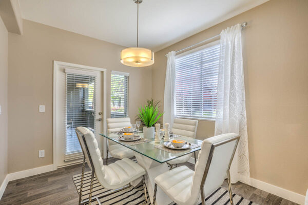 Dining room with glass table, plush leather chairs, light fixture, and large windows.