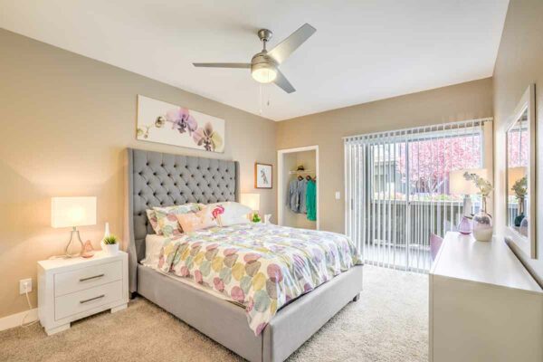 Bedroom with carpet, plush bed with headboard, bedside tables with lamps, and sliding balcony door.
