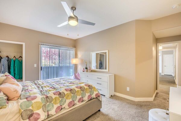 Bedroom with carpet, plush bed, dresser with mirror, and doors to hallway and balcony.