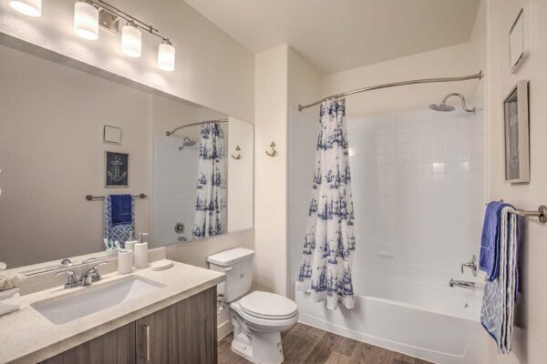 Bathroom with wood cabinets, light counters, large mirror, and tiled shower tub.