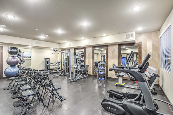 Fitness center with cardio machines, weight equipment, large mirrors, and fitness chairs.