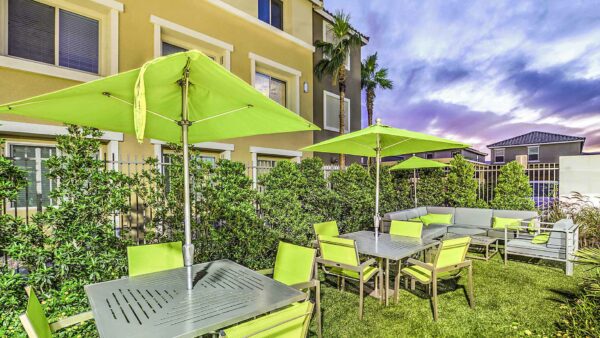 Outdoor seating area with outdoor sectional, dining tables with umbrellas, and lush landscaping.