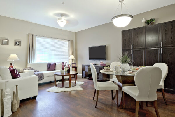 Living area with glass dining table, leather chairs, wood cabinets, TV, and large window.