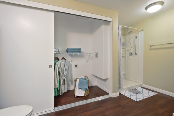 Bathroom with wood floor, large closet with shelves and clothes, and tiled shower.