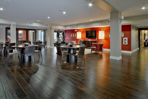 Lounge with wood tile floor, dining tables with chairs, red accent walls, and console with TV.