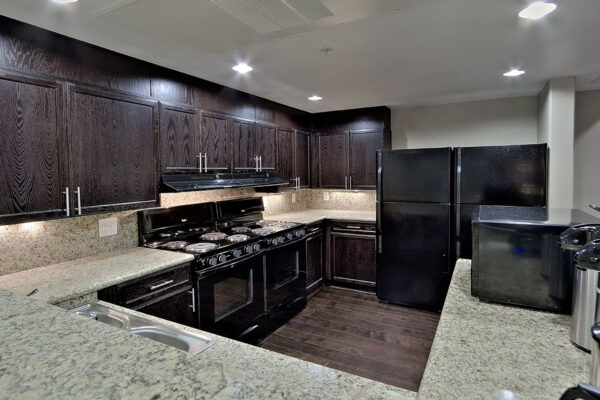Demo kitchen with wood floor and cabinets, stone counters, and black appliances.