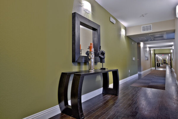 Hallway with wood tile floor, large framed mirror, table with decor, and green accent walls.