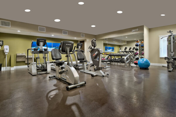 Fitness center with cardio machines, weight equipment, mirror walls, and drinking fountains.
