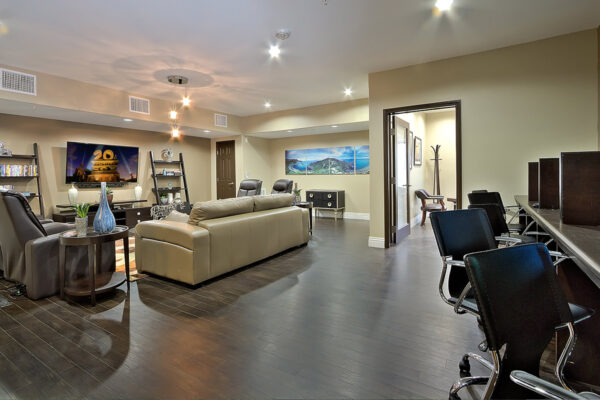 Lounge with computer desks, plush leather seating, large TV, and shelves with decor.