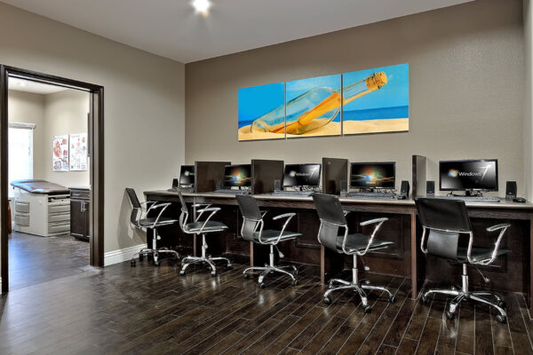 Business center with wood tile floor, computer desks with chairs, and large triptych artwork.