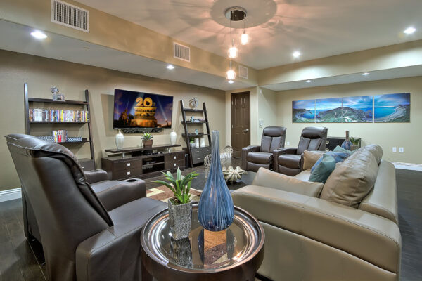 Movie lounge with plush leather chairs, shelves with decor and movies, and large TV.
