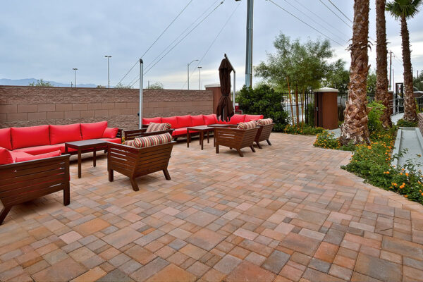 Outdoor lounge with stone paver patio, lounge chairs, plush sectional, lush landscaping, and tall palms.