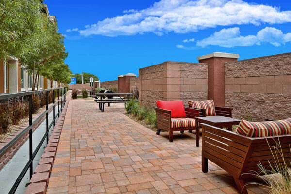 Outdoor lounge with stone paver patio, lounge chairs, picnic tables, BBQ grills, and lush landscaping.