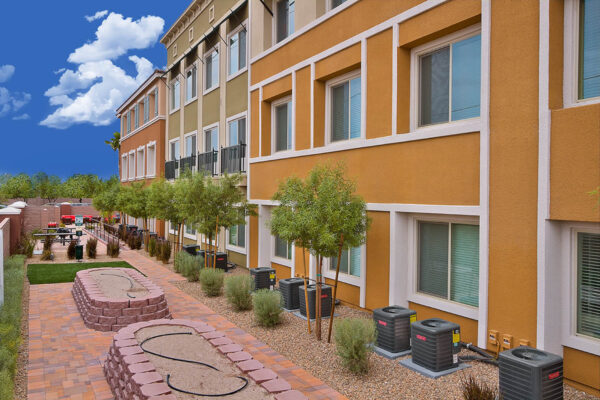 Outdoor lounge with stone paver patio, lounge chairs, picnic tables, BBQ grills, and lush landscaping.
