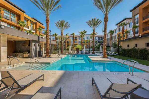 Aspire at Flamingo Grand apartments pool area with lounge chairs and tall palm trees.