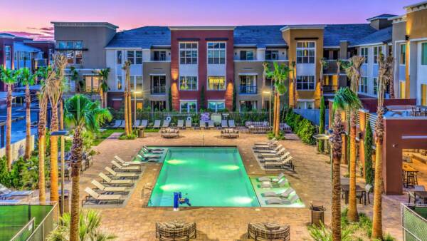 Aspire at Tropicana pool area with lounge chairs, dining tables, daybeds, stone paver patio, and tall palm trees.