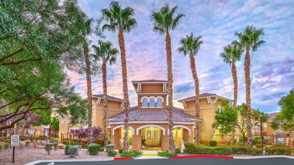 Chateau Calais office entrance with elegant architecture, lush landscaping, and tall palm trees.