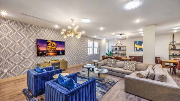 Tesora community lounge with plush seating, pattern wallpaper, TV, and sculptured chandelier.
