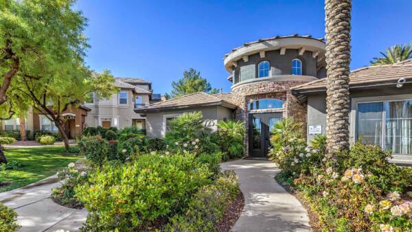 Tuscany apartment clubhouse with classic architecture, lush landscaping, and tall palm trees.