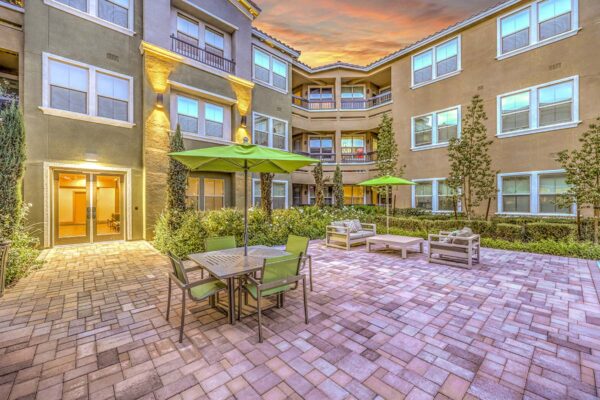Courtyard with stone paver patio, dining table with umbrellas, outdoor lounge chairs, and lush landscaping.
