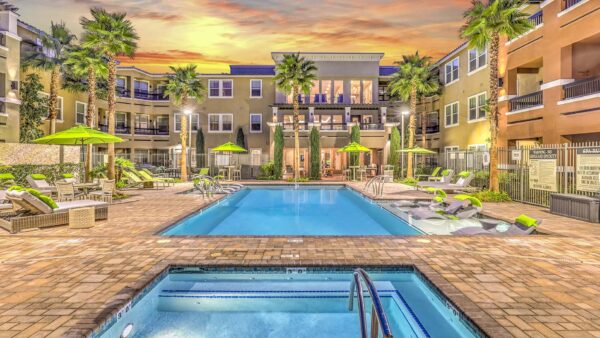 Pool area with hot tub, lounge chairs, umbrellas, lush landscaping, and tall palm trees.