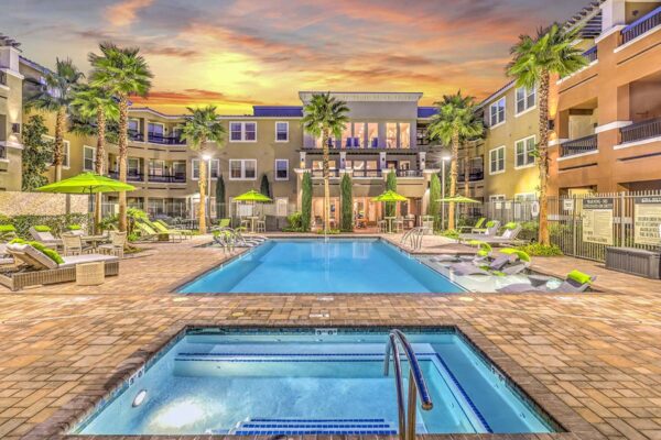 Pool area with hot tub, lounge chairs, umbrellas, lush landscaping, and tall palm trees.