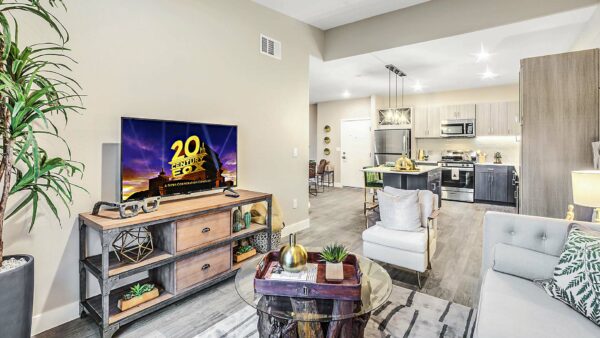 Living room with plush seating, industrial shelves with TV, and glass coffee table with decor.