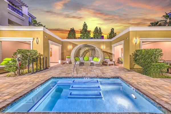 Indoor/outdoor lounge with hot tub, cabana with plush seating, and stone paver patio.