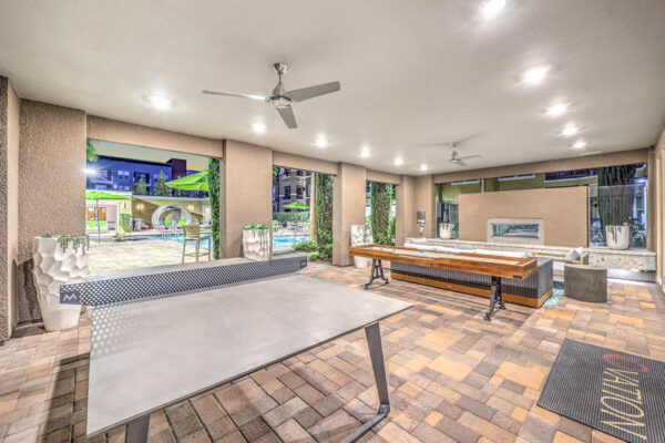 Indoor/outdoor lounge with stone paver patio, game tables, plush seating, and fireplace.