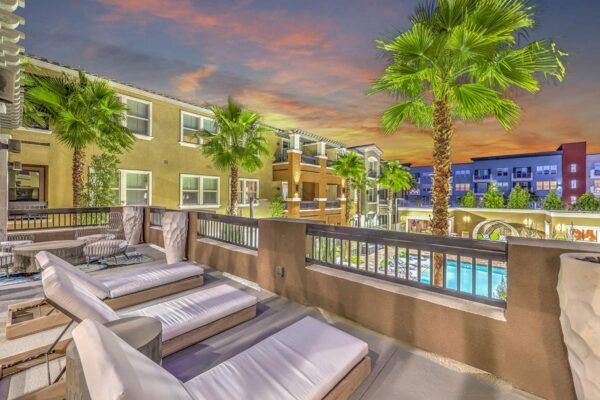 Rooftop patio with lounge chairs, large potted plants, and metal railing overlooking pool area.