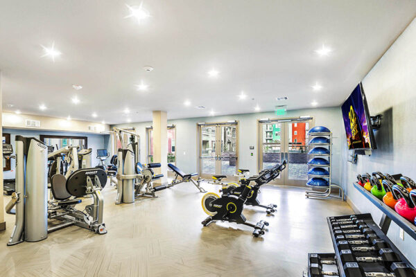 Fitness center with cardio machines, weight equipment, TV, and doors to courtyard.
