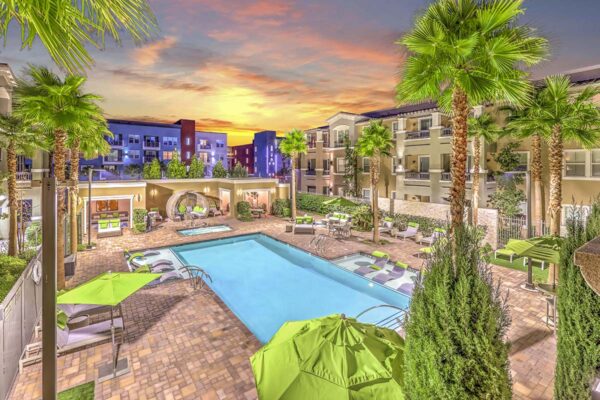 Overhead view of pool area with lounge chairs, umbrellas, gazebo, and tall palm trees.