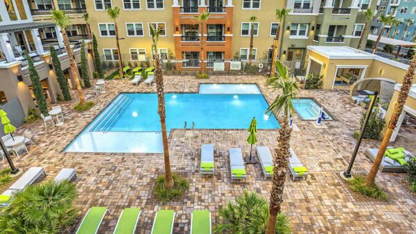 Overhead view of pool area with lounge chairs, daybeds, umbrellas, dining tables, and tall palms.