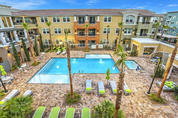 Overhead view of pool area with lounge chairs, daybeds, umbrellas, dining tables, and tall palms.