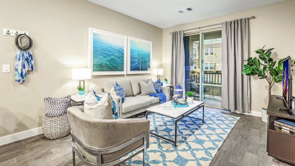 Living room with wood floor, plush seating, framed artwork, and sliding door to balcony.