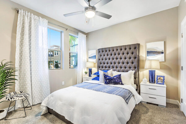 Bedroom with carpet, plush bed with headboard, bedside drawers with lamps, and large window.